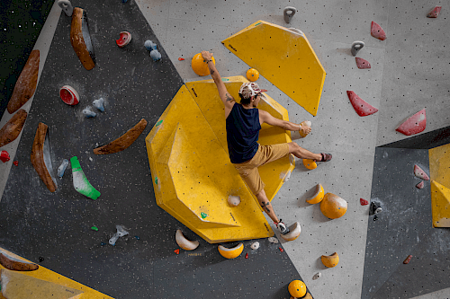 Mann klettert an einer Boulderhalle mit bunten Elementen