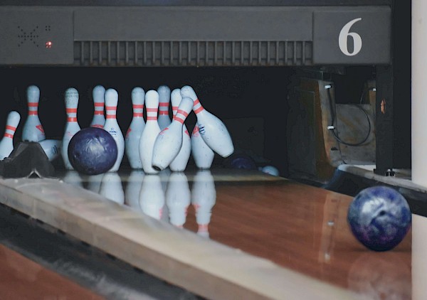 Ende einer Bowlingbahn mit umgeworfenen Pins und zwei Bowlingkugeln.