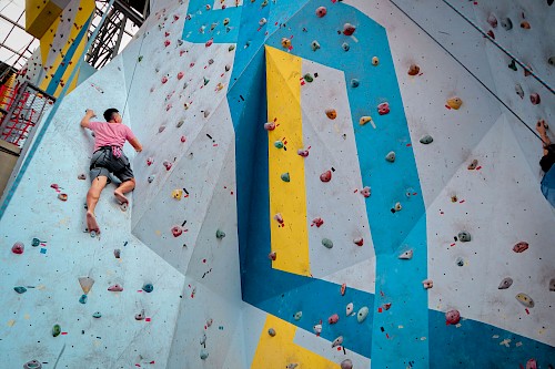 Mann mit rotem T-Shirt, der an einer bunt bemalten Kletterhallenwand hängt